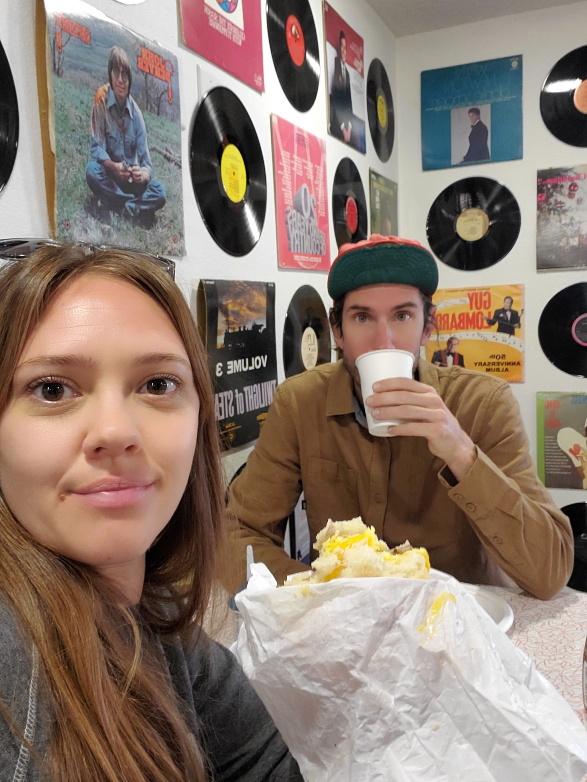 Couple having coffee in front of a wall decorated with classic records at Expedition Lodge.